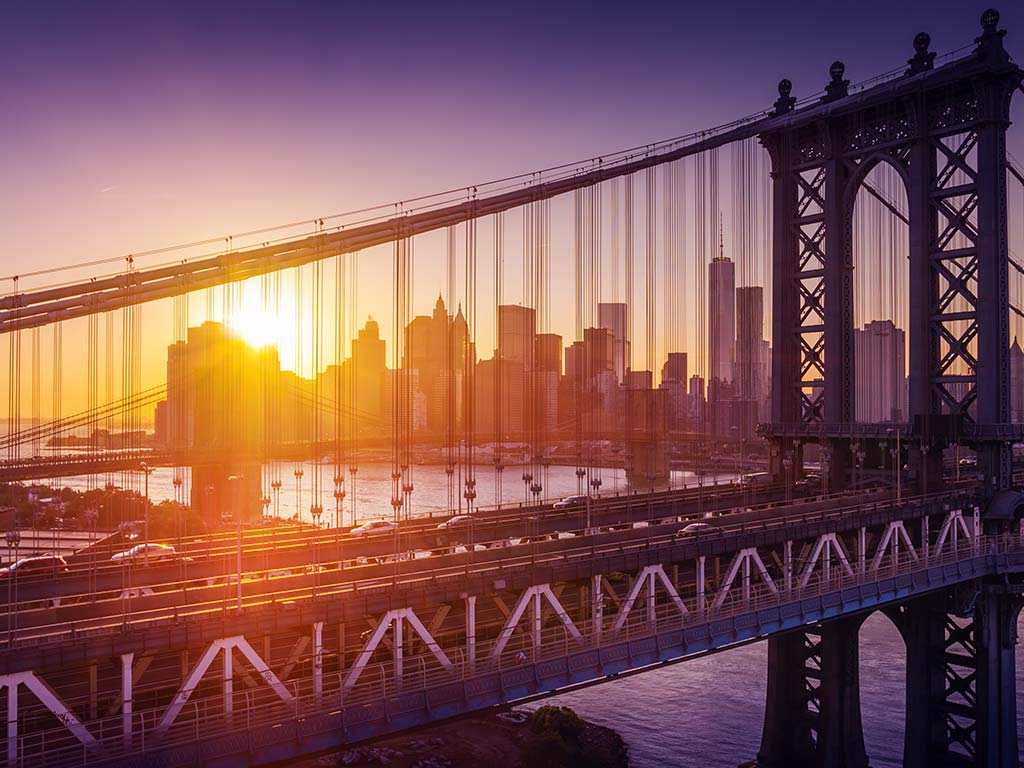 Bridge with New York city skyline in the background at sunset